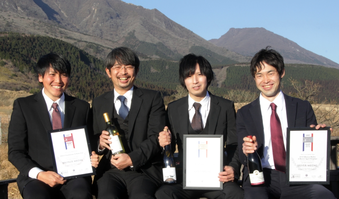 海外品評会で入賞したワインを手にする土持浩嗣支配人（左から３人目）と社員たち＝竹田市久住町